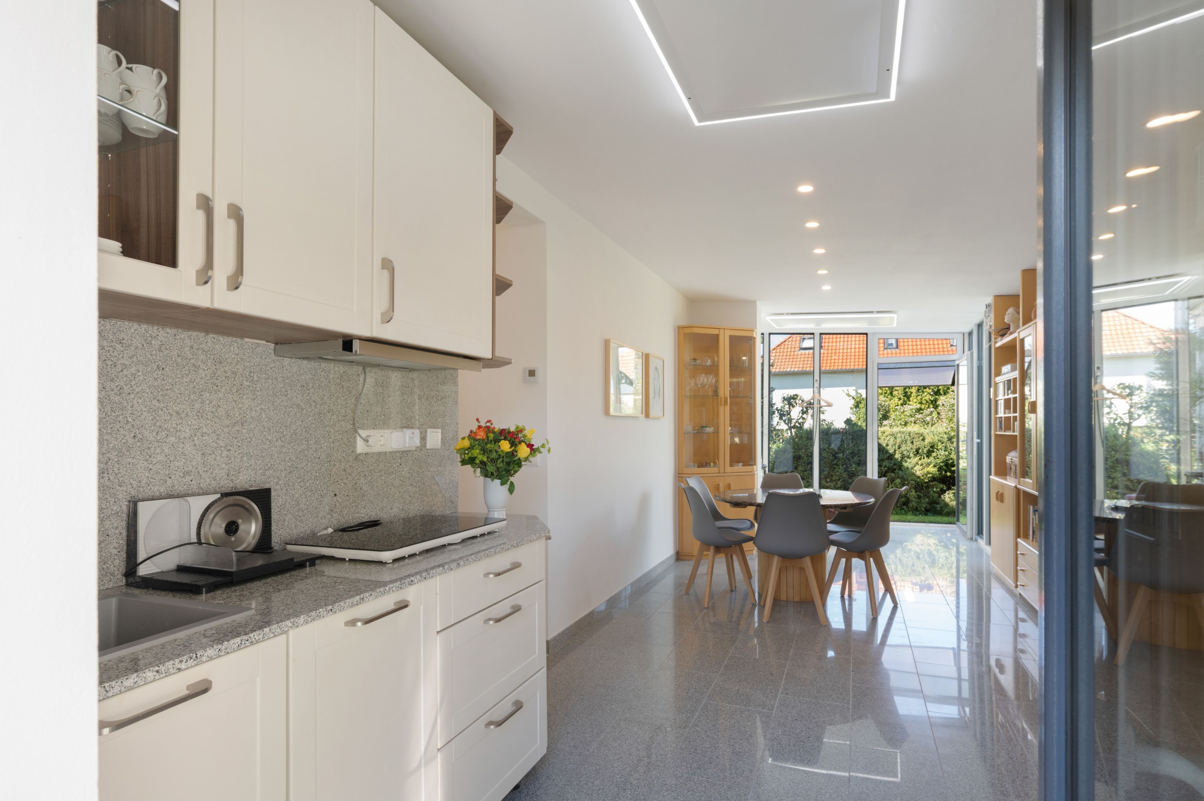A modern kitchen with granite countertops, white cabinetry, and a dining area with a glass door leading to a garden.