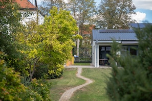 A pathway leading to a building with a metal roof, surrounded by greenery and trees.