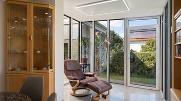 Een moderne kamer met een glazen kast, een lederen fauteuil en uitzicht op het groen.
