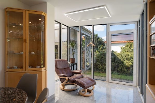A modern room with a glass cabinet, a leather chair, and a view of the outdoors.