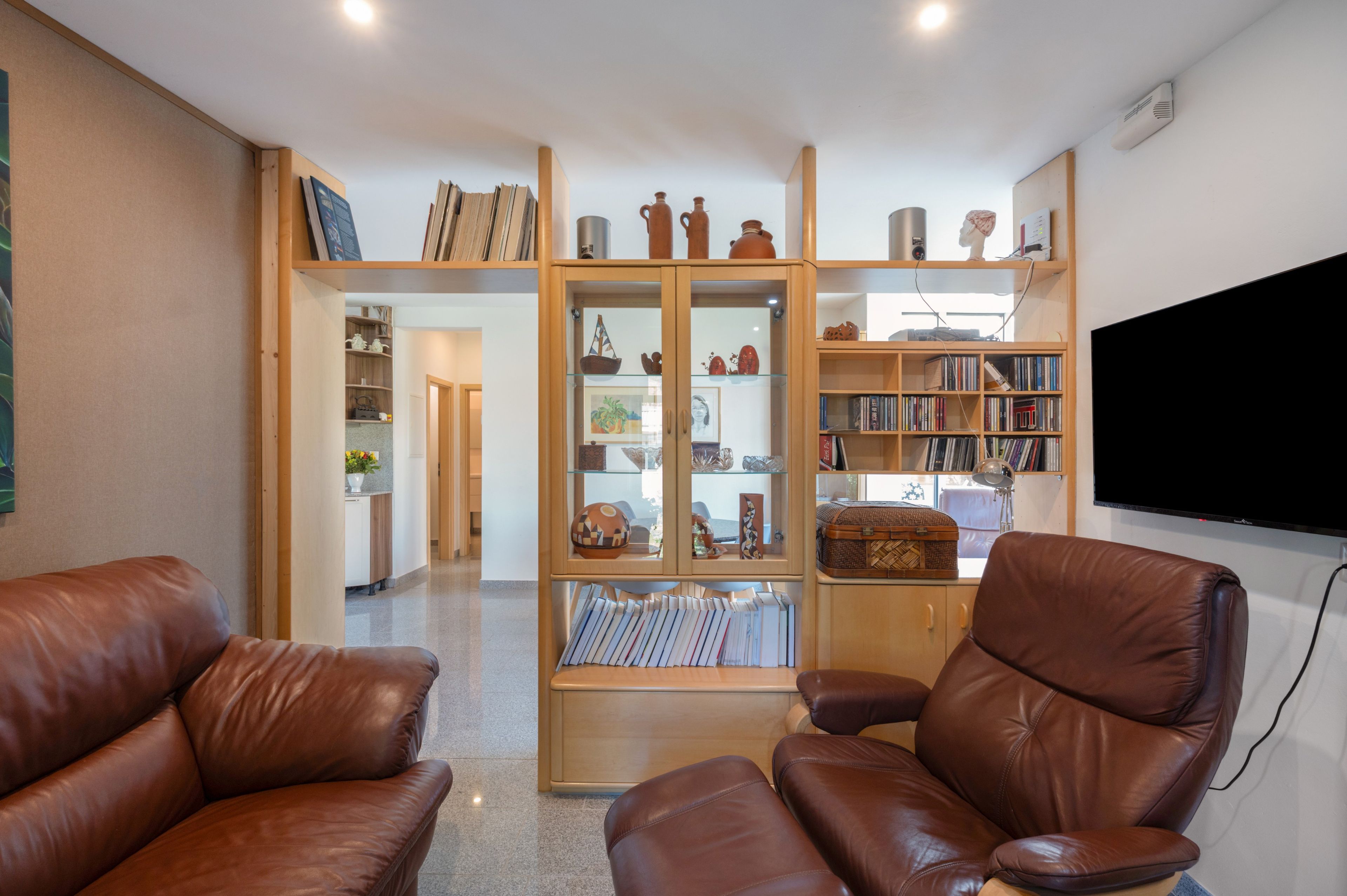 A living room with leather armchairs, a wooden bookshelf, and a flat-screen TV.