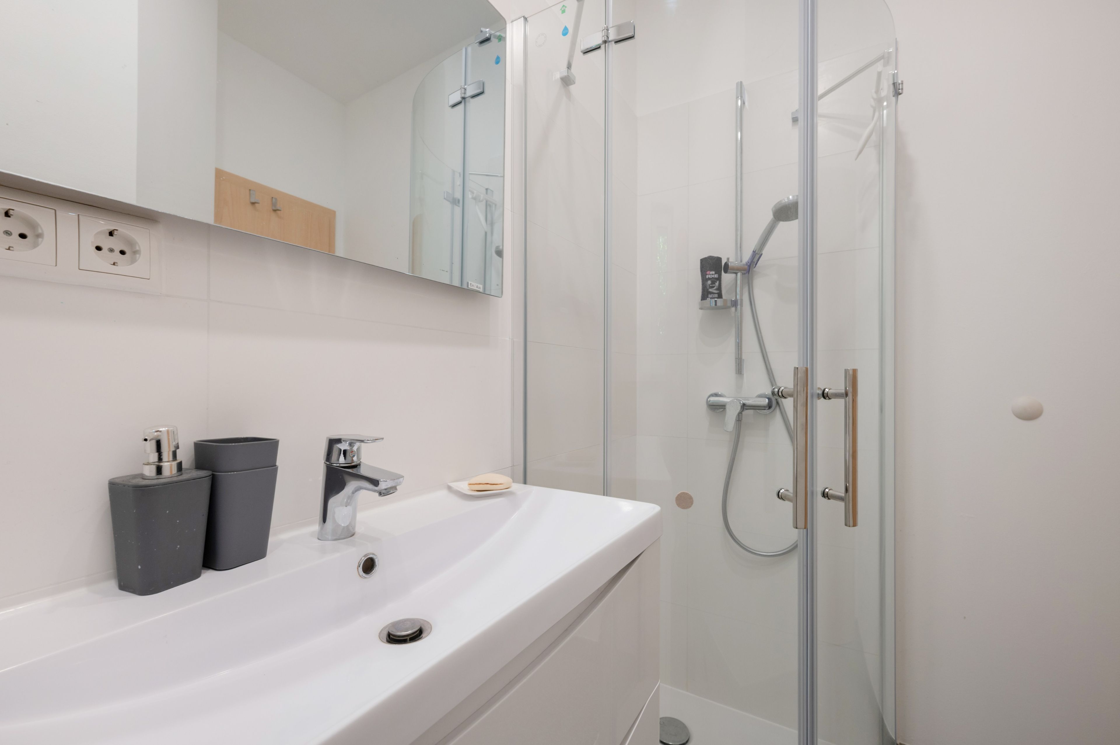 Ein modernes Badezimmer mit Waschbecken, Spiegel, Duschkabine und Handtuchhalter.