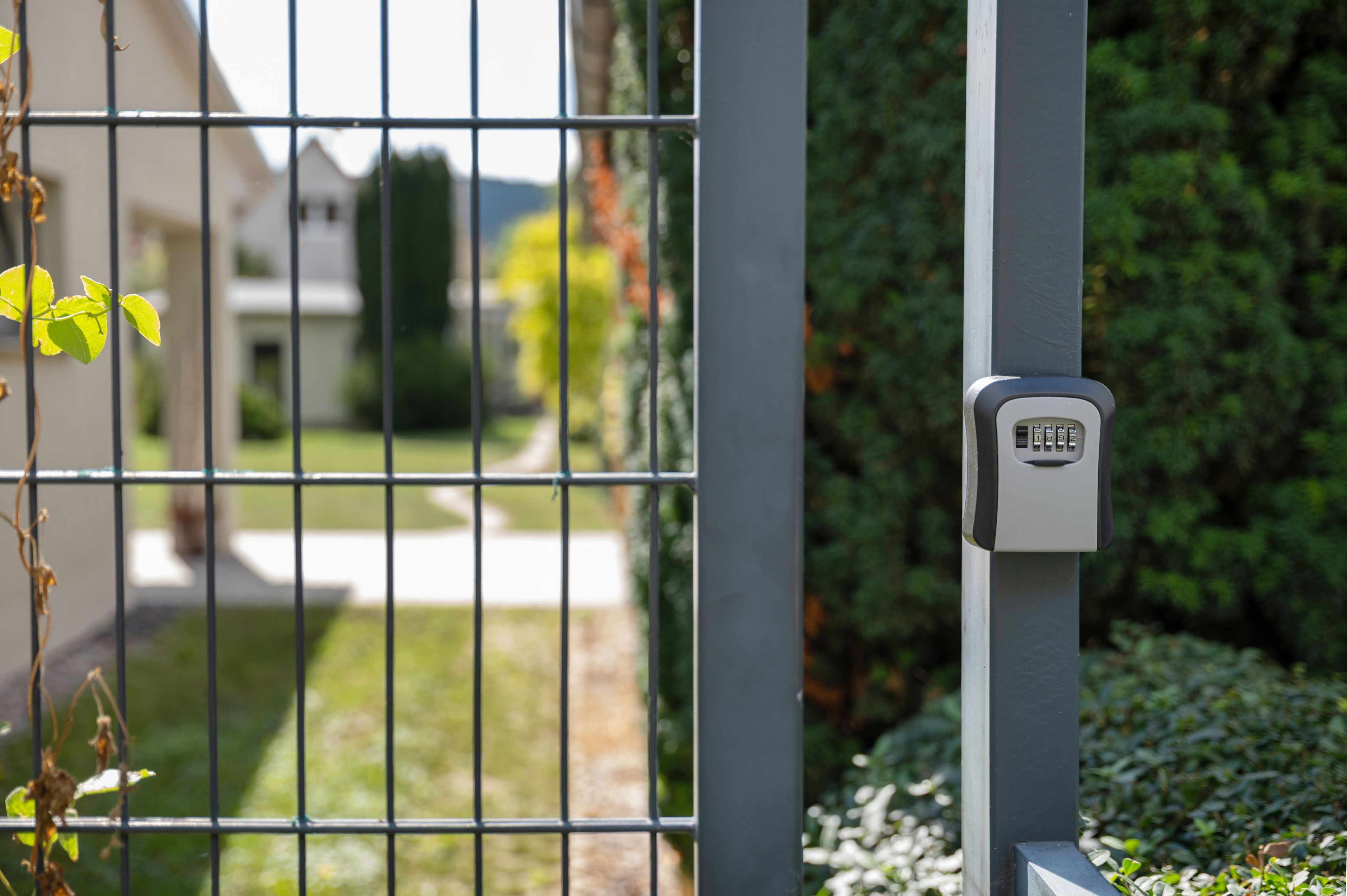 Ein Metallzaun mit Zahlenschloss, ein klarer Weg zu einem Haus und ein gepflegter Rasen.