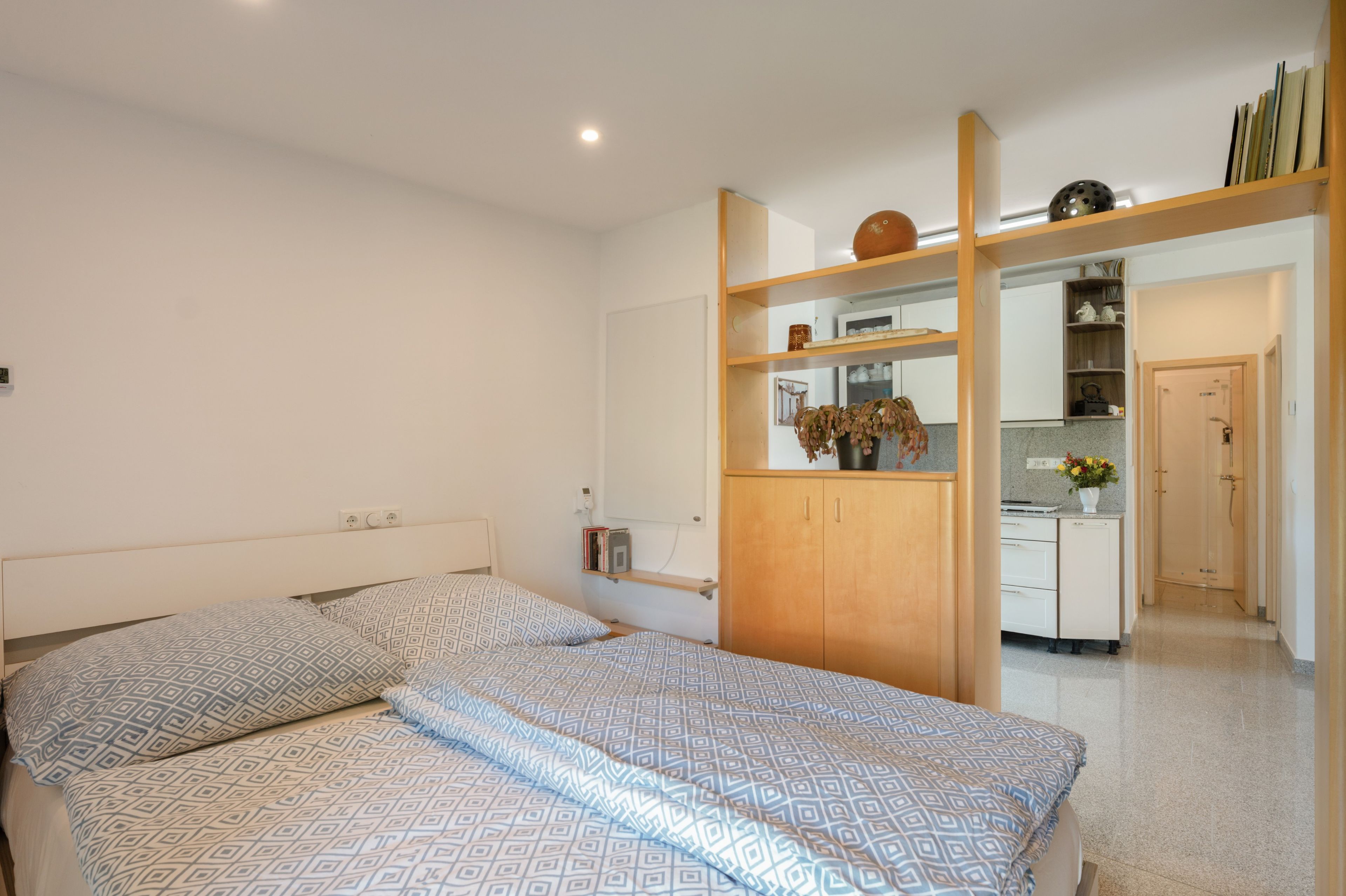 Ein Schlafzimmer mit einem Bett, Nachttischen, einem Kleiderschrank und einem durch eine offene Tür einsehbaren Küchenbereich.