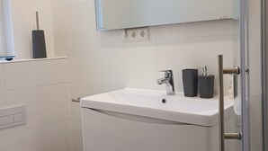 Casa de banho moderna com lavatório branco, espelho e sanita.