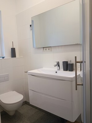 Ein modernes Badezimmer mit einem weißen Waschbecken, Spiegel und WC.