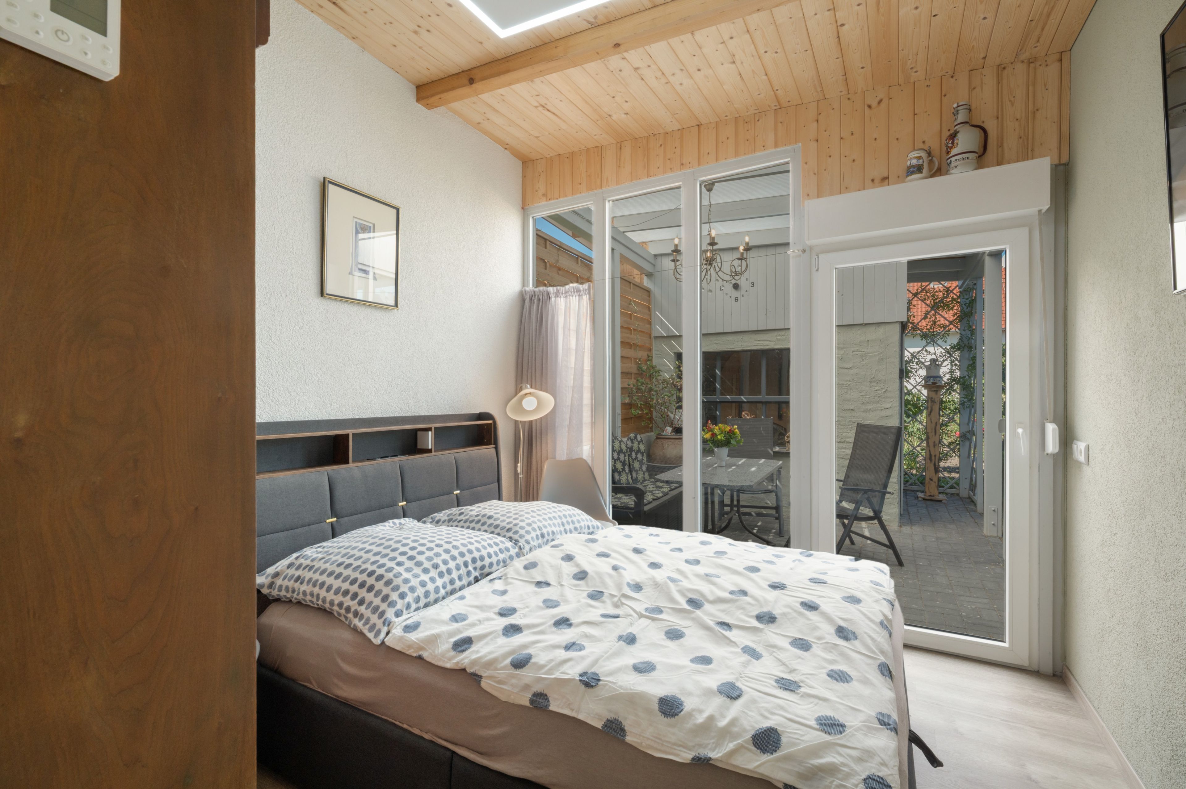 A bedroom with a bed, a bedside table, a chair, and a view of an outdoor patio area.