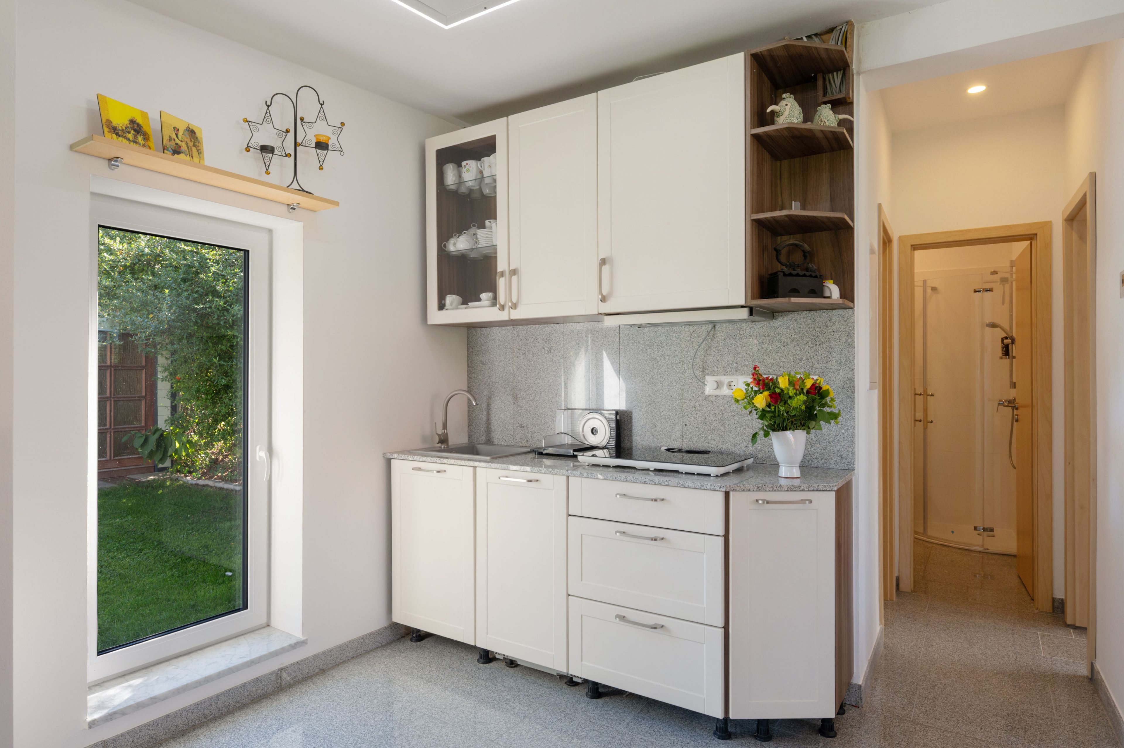 A modern kitchen with white cabinetry, a built-in oven, and a window overlooking a garden.
