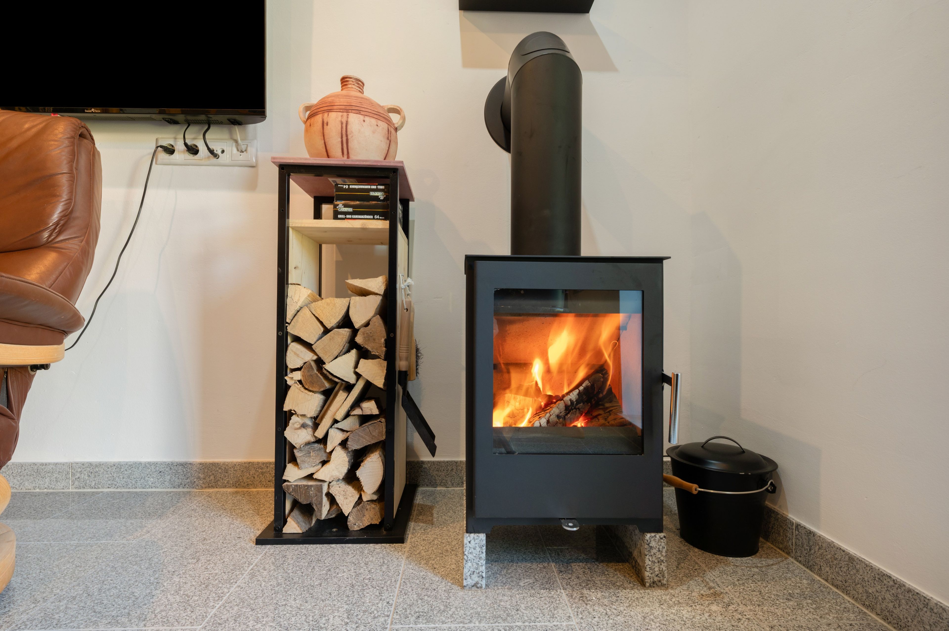 Ein Holzofen mit Feuer, ein Holzstapel und ein an der Wand befestigter Fernseher.