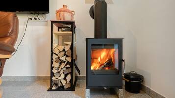 Ein Holzofen mit Feuer, ein Holzstapel und ein an der Wand befestigter Fernseher.
