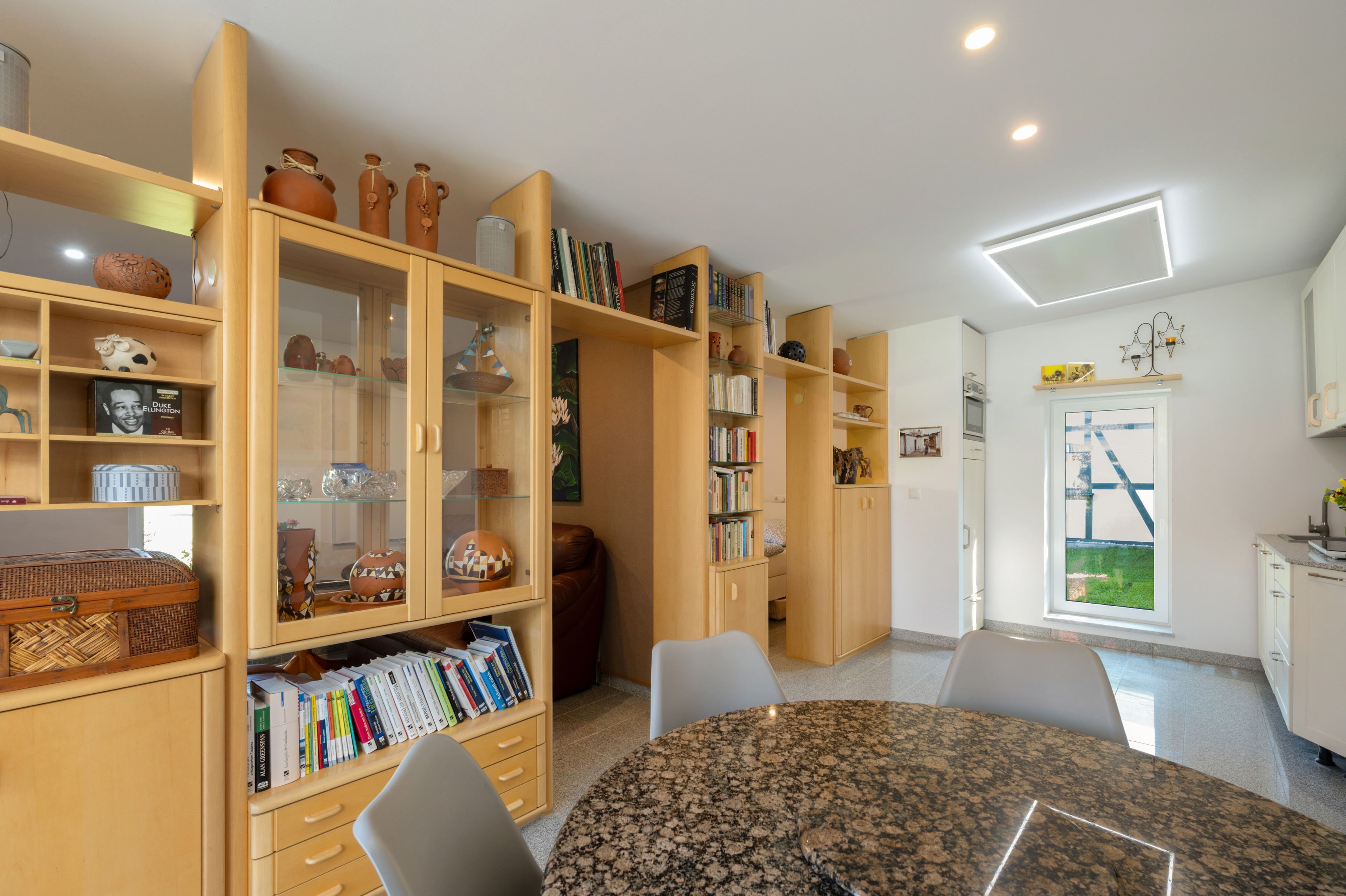 Een goed verlichte kamer met een ronde tafel, boekenkasten en een raam met uitzicht.