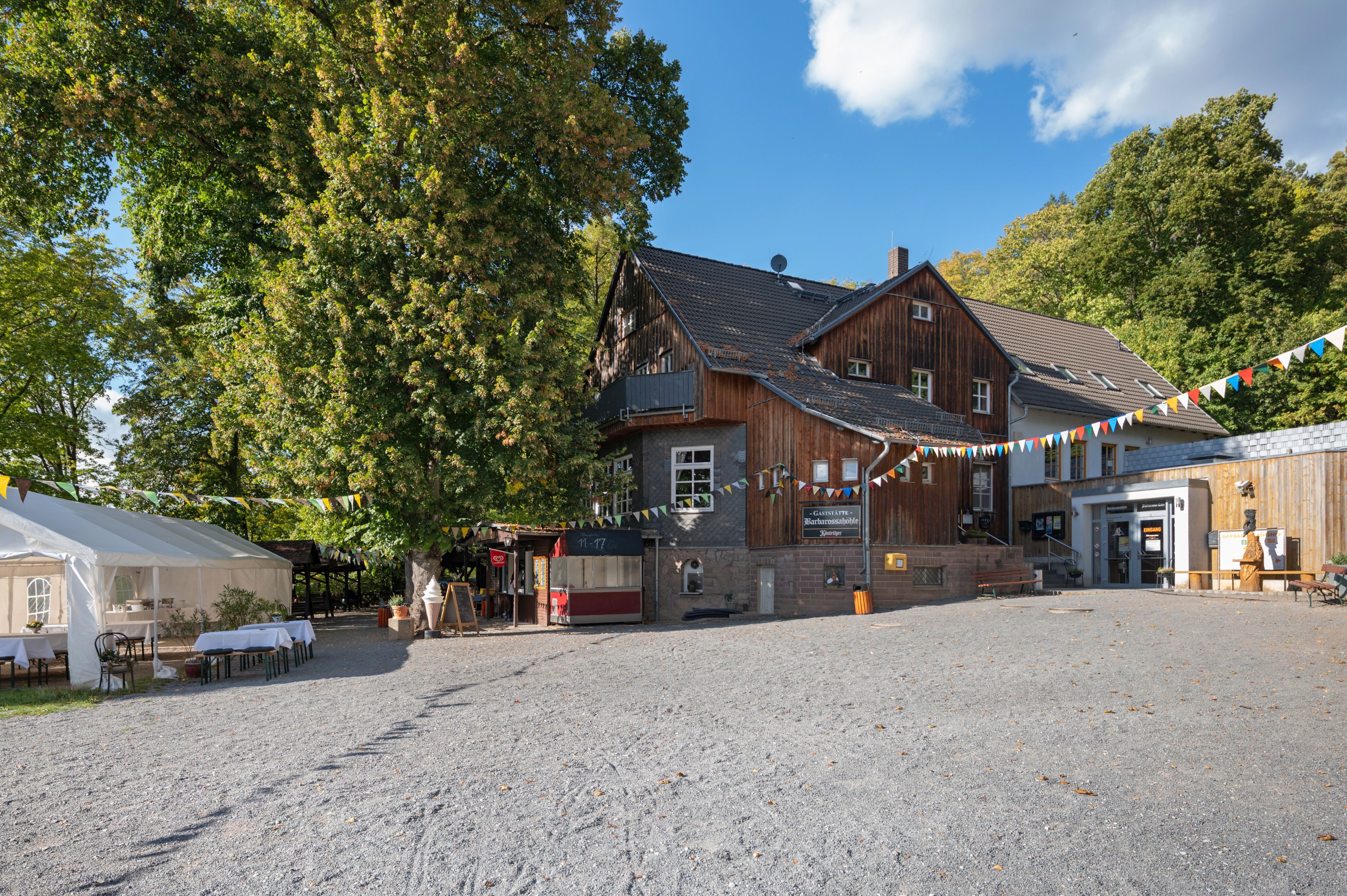 Ein traditionelles Holzgebäude mit Kieshof, umgeben von Bäumen.