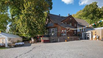 Ein traditionelles Holzgebäude mit Kieshof, umgeben von Bäumen.