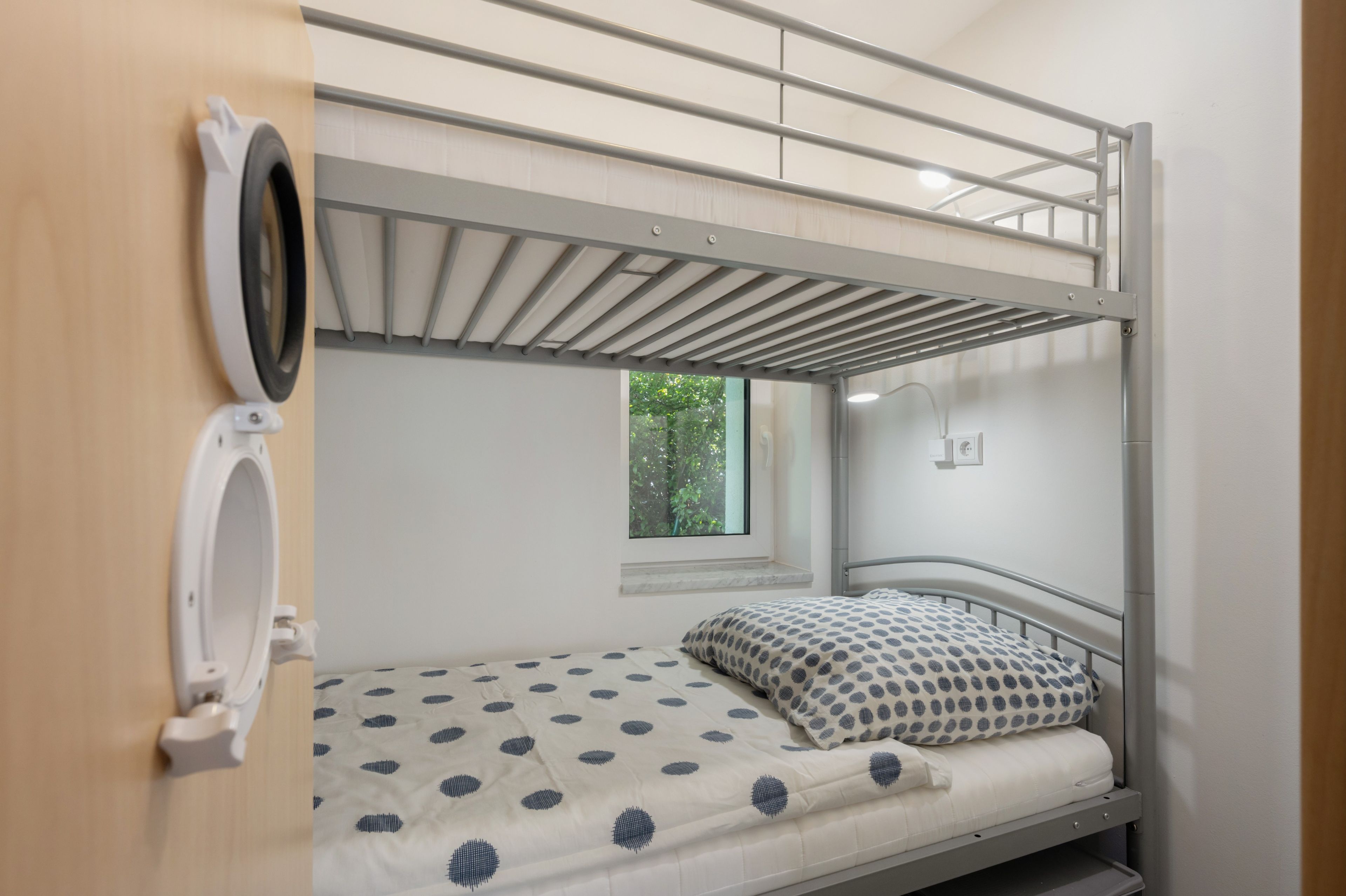 Ein Etagenbett mit Fenster, einer kleinen Ablagefläche und einer wandmontierten Leuchte.