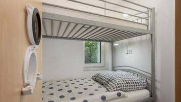 Ein Etagenbett mit Fenster, einer kleinen Ablagefläche und einer wandmontierten Leuchte.