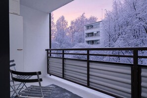 Ein Balkon mit Metallgeländer, einem Stuhl und Blick auf ein Gebäude mit schneebedeckten Bäumen.