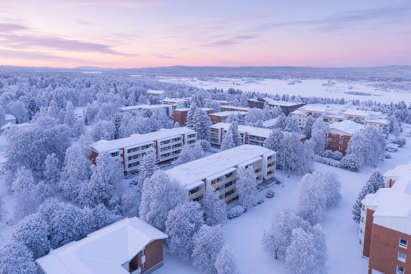 A snow-covered residential area with multiple apartment buildings and trees.