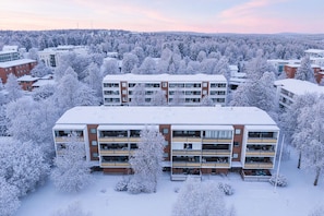 Ein mehrgeschossiges Wohngebäude mit flachem Dach, umgeben von schneebedeckten Bäumen und weiteren Gebäuden.