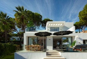 Ein modernes, zweistöckiges Haus mit Terrasse, Sitzgelegenheiten im Freien und Blick auf die umliegende Natur.