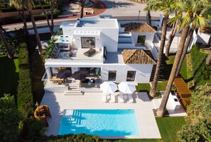 Ein modernes, zweistöckiges Haus mit Swimmingpool, Sitzgelegenheiten im Freien und einem gepflegten Garten.