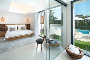 Ein modernes Schlafzimmer mit einem großen Bett, einer Glastür zum Poolbereich und Blick ins Freie.