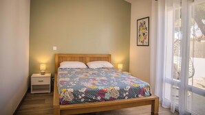 Un dormitorio con cama de madera, dos lámparas de noche, una mesita de noche, una ventana con cortinas y un cuadro colgado en la pared.