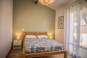 Un dormitorio con cama de madera, dos lámparas de noche, una mesita de noche, una ventana con cortinas y un cuadro colgado en la pared.