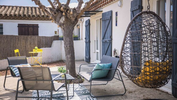 Un área de estar al aire libre con sillas y una sillona colgante en forma de huevo, un árbol y un edificio con techo de tejas.