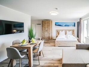 A modern hotel room with a wooden bed, a dining area with a table and chairs, and a large window providing a view of the outdoors. - Holiday Apartment 708 (Winterberg)