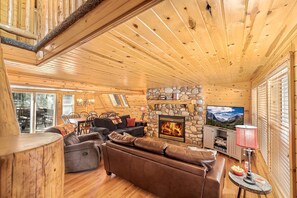 Ein Holzblockhaus-Interieur mit Kamin aus Stein, Ledersofas, einem Fernseher und einem Essbereich.