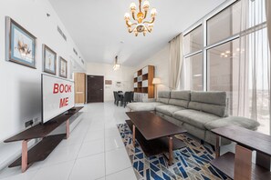 A modern living room with a sofa, a coffee table, a TV, and a chandelier. - StayShort - Peaceful 2-bedroom in Al Furjan that Sleeps 6! (Al Furjan)