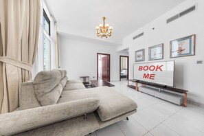 A modern living room with a sofa, a TV, and a chandelier. - StayShort - Peaceful 2-bedroom in Al Furjan that Sleeps 6! (Al Furjan)