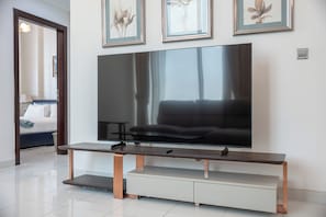 A modern living room with a large flat-screen TV mounted on a wooden stand, a sofa, and a coffee table. - StayShort - Peaceful 2-bedroom in Al Furjan that Sleeps 6! (Al Furjan)