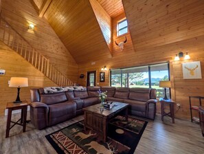 A spacious living room with a leather sectional sofa, a coffee table, and a staircase. - Fresh Summer Cabin with Hot Tub, Firepit & Outdoor BBQ in Island Park, Idaho (Island Park)