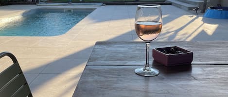 A poolside table with a glass of wine, a chair, and a bowl of nuts.