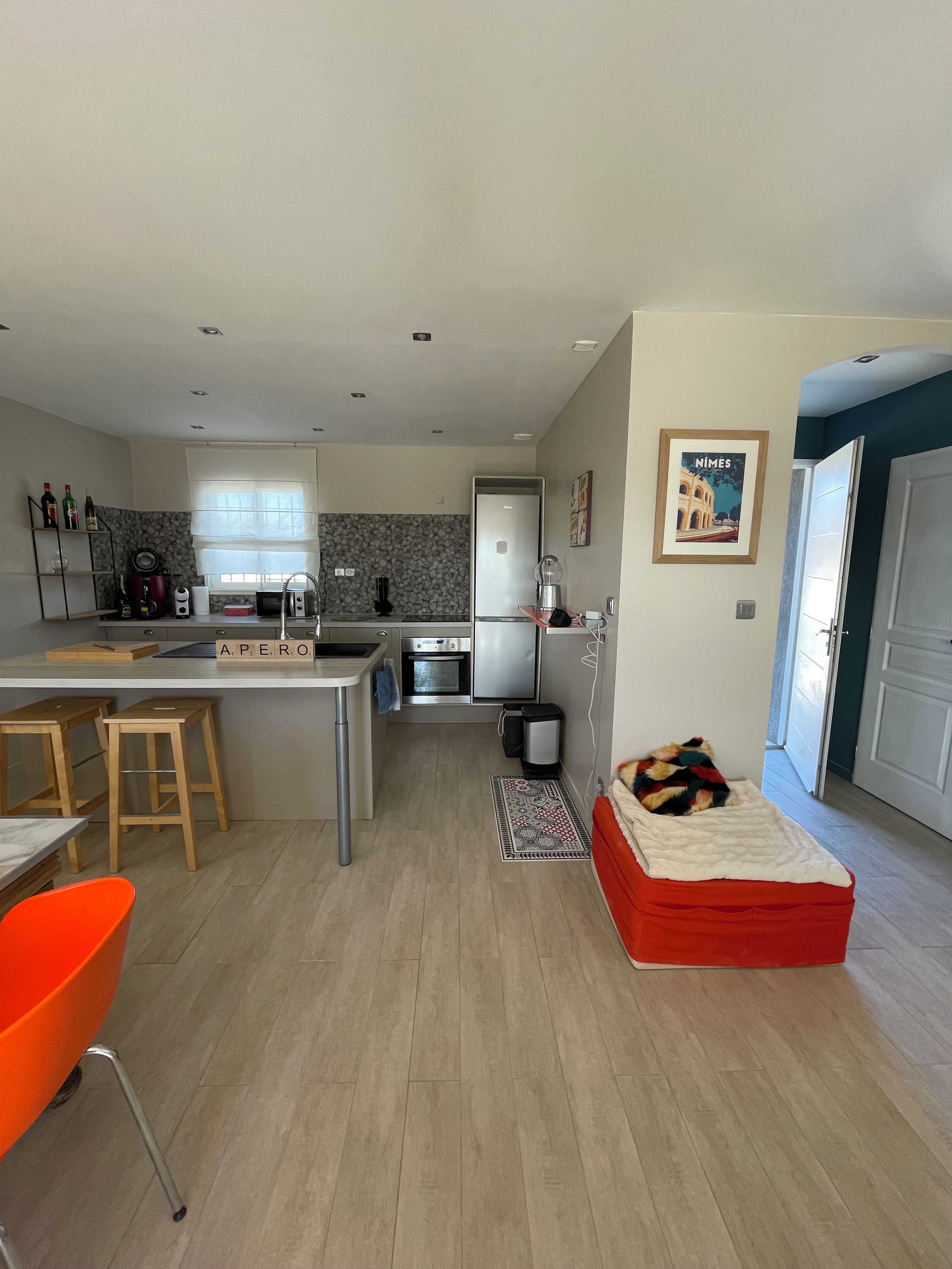 A modern kitchen with a dining area, a small sofa, and a red ottoman.