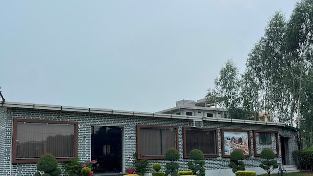 A building with a brick facade, large windows, and a well-maintained lawn with trimmed bushes. - Farmgrill Restaurant And Party Lawn (Haldwani)