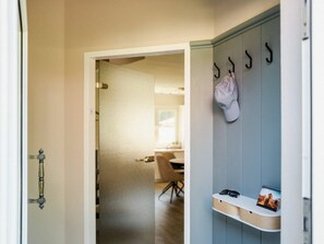 Ein Zimmer mit einer zur Diele führenden Tür, einem Kleiderständer mit Hut und einem Regal mit Zeitschrift und Brille.