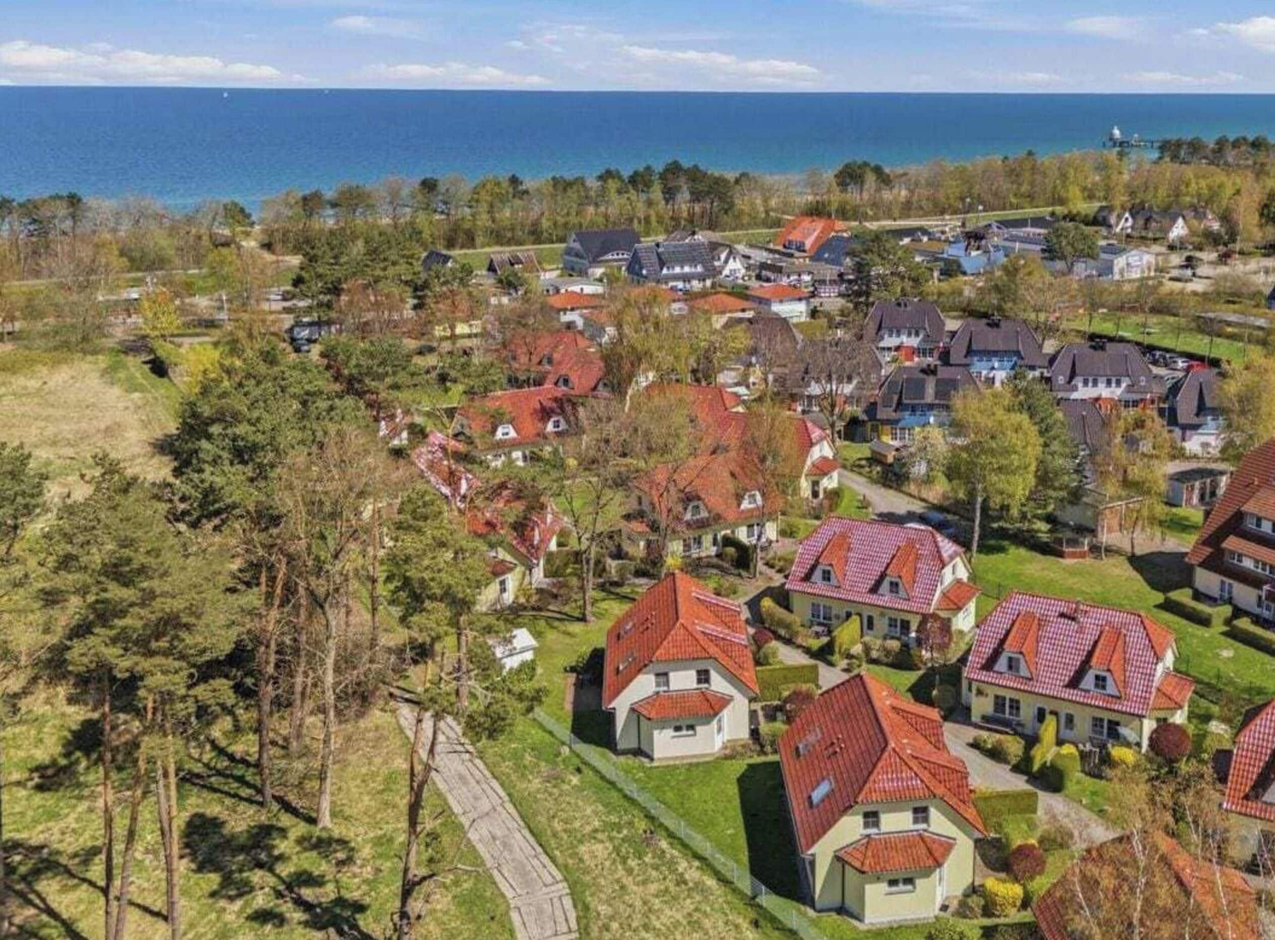 Un barrio residencial con casas de techos rojos, rodeado de vegetación y vistas al mar.