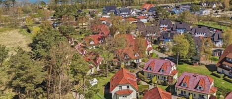 A residential area with houses having red roofs, surrounded by greenery and a view of the sea.