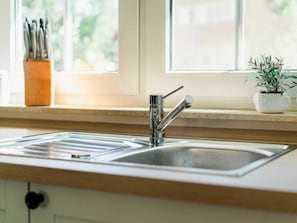 A kitchen with a stainless steel sink, a window with a view of greenery, and a potted plant on the windowsill. - At the Dike, House Number 26 (Ostseebad Zingst a Darss)