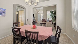 A dining area with a round table, chairs, and a chandelier. There is a door leading to another room, and a plant is visible in the background. - Spacious 6-BR Furnished 30 day rental! Great Pool! (Chandler)