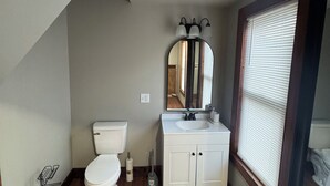 A bathroom with a toilet, sink, mirror, and window with blinds. - The Walnut Inn, 2BR Handicap-Accessible Apt. Located in Parsons; Pet Friendly (Parsons)