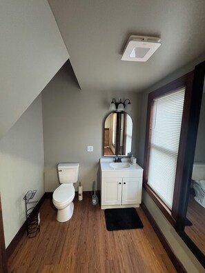 Un baño con inodoro, lavabo, espejo y ventana con persianas.
