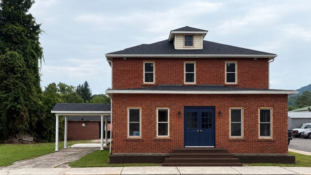A two-story brick house with a dark blue front door, a covered porch, and a garage. - The Walnut Inn, 2BR Handicap-Accessible Apt. Located in Parsons; Pet Friendly (Parsons)