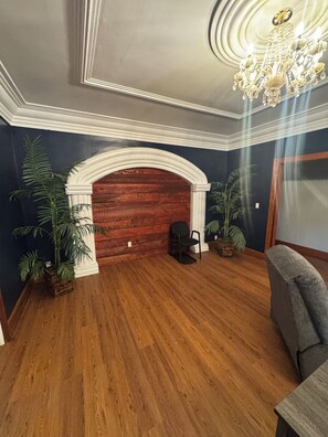 A room with a wooden floor, a fireplace, a chandelier, and two potted plants. - The Walnut Inn, 2BR Handicap-Accessible Apt. Located in Parsons; Pet Friendly (Parsons)