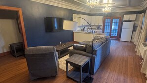 A living room with a sectional sofa, a small table, and a TV mounted on the wall. - The Walnut Inn, 2BR Handicap-Accessible Apt. Located in Parsons; Pet Friendly (Parsons)