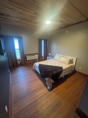 A bedroom with a bed, a nightstand, a lamp, a window with curtains, and a ceiling fan. - The Walnut Inn, 2BR Handicap-Accessible Apt. Located in Parsons; Pet Friendly (Parsons)
