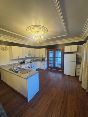 A spacious kitchen with a central island, white cabinetry, a chandelier, and a double door leading to an outdoor area. - The Walnut Inn, 2BR Handicap-Accessible Apt. Located in Parsons; Pet Friendly (Parsons)