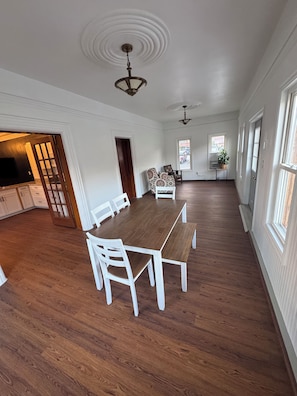 Una habitación amplia con una mesa de comedor de madera, sillas blancas y un ventilador de techo.